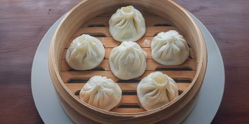 Six steamed dumplings in a bamboo basket on a wooden table.