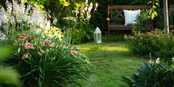 A serene garden pathway with blooming flowers and a wooden bench.