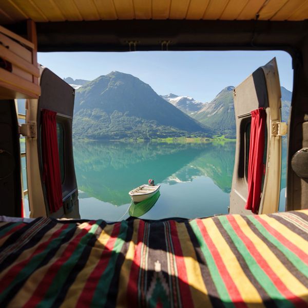 View of a serene lake and mountains from inside a camper van with open doors.