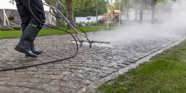Person pressure washing a cobblestone path.
