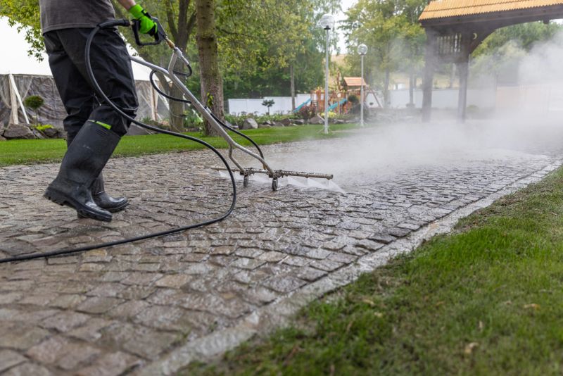 Professional cleaning service worker power washing cobblestone driveway with high pressure washer