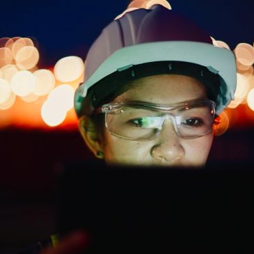 Worker in safety gear focused on a tablet at night.