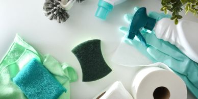 Assorted cleaning supplies including sponges, gloves, sprays, and toilet paper on a white surface.