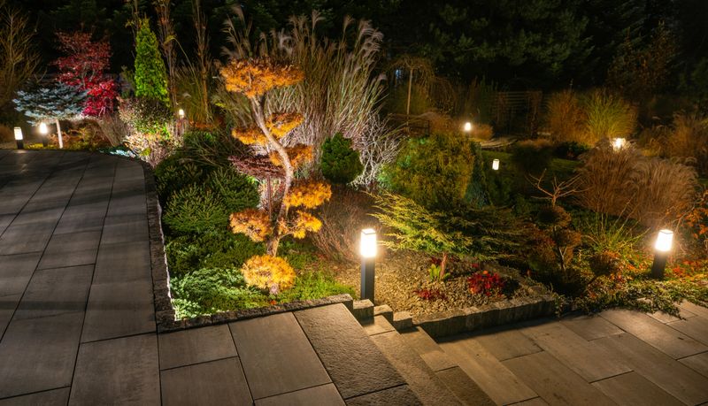 Warm lights illuminate the garden pathway, highlighting vibrant trees and manicured plants