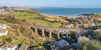 Scenic coastal town with an old stone viaduct and lush green fields under a clear blue sky.