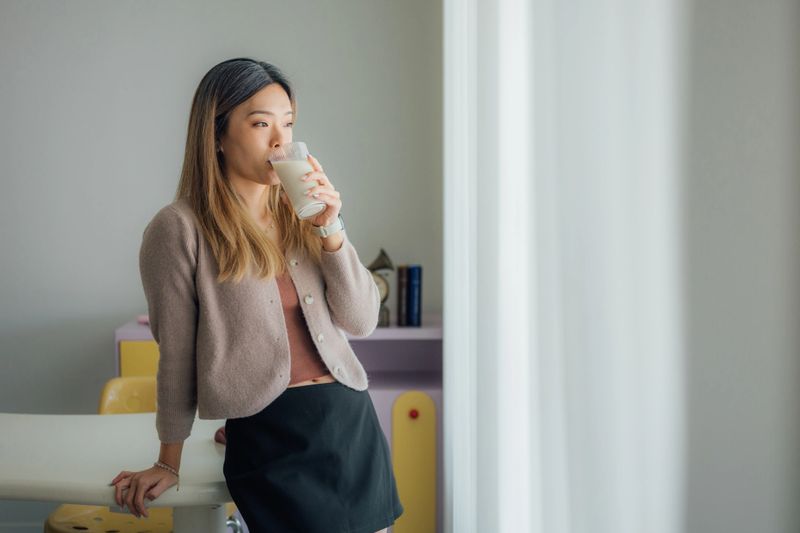 A beautiful young Asian Chinese woman is enjoying drinking milk, as it provides calcium and energy to the body, while relaxing in the living room at home.