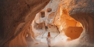 Person exploring ancient rock-cut caves illuminated by warm sunlight.