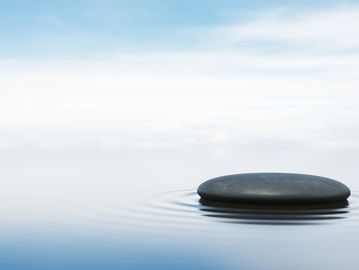 A smooth stone resting on calm water with gentle ripples.
