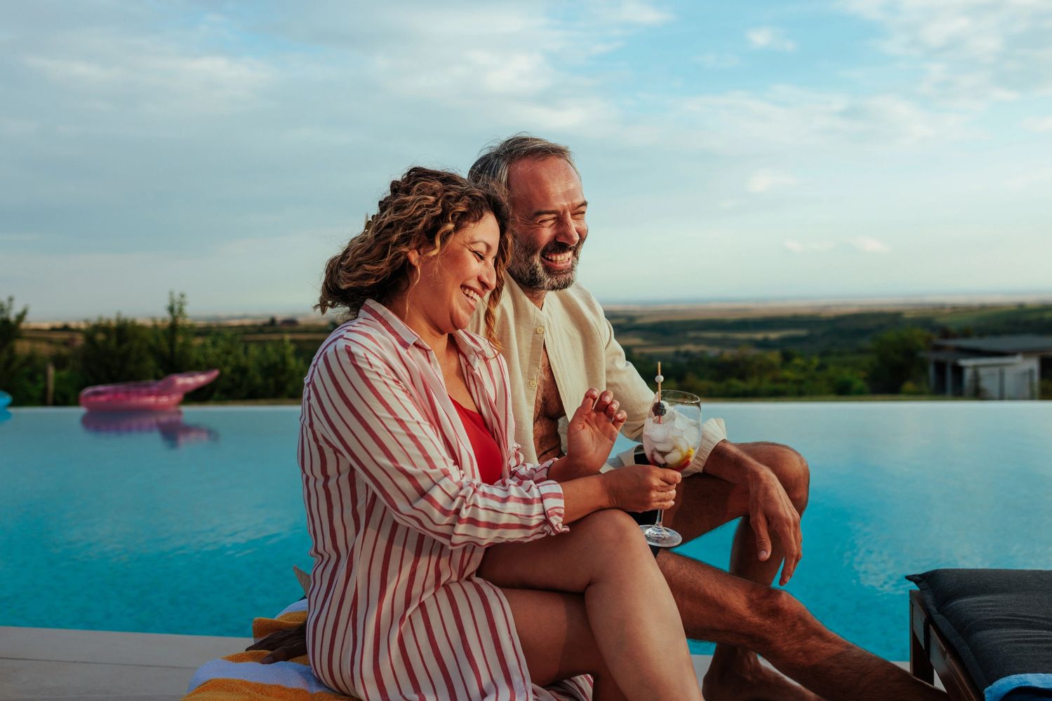 A happy couple relaxes by an infinity pool, enjoying drinks and each other's company.