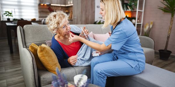 Caregiver assisting elderly woman with medicine at home.