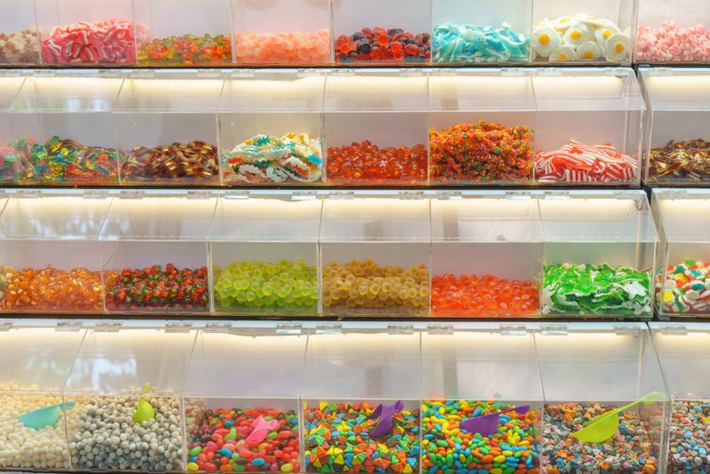 Rows of transparent bins filled with a variety of colorful candies, including gummies, hard candies, licorice, and chocolate-coated treats. The vibrant display showcases a delightful mix of textures and flavors, perfect for sweet lovers and retail shops.