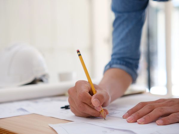 Person sketching or drafting on paper with a pencil on a wooden table.