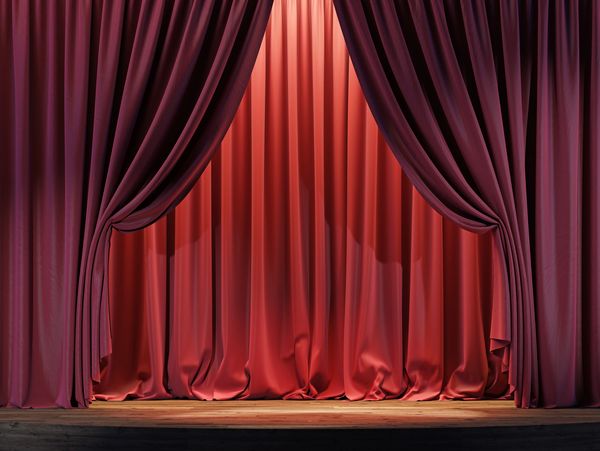 A stage with red curtains partially drawn, illuminated by warm lighting.
