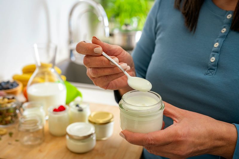 Close up of woman hands holding a spoon and container freshly prepared  homemade yogurt