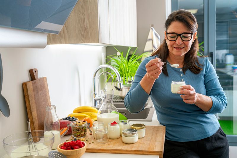 Mature woman eating freshly prepared  homemade yogurt in the kitchen