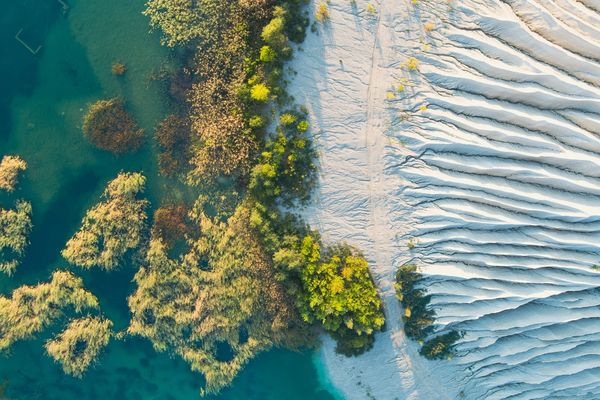 Aerial view of water, green plants, and sand dunes.