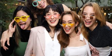 Five friends wearing funky sunglasses, smiling and posing outdoors.