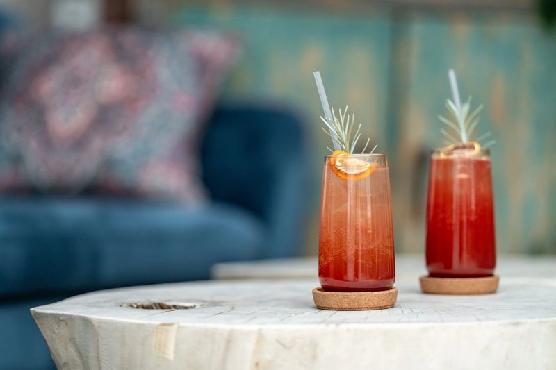 Two vibrant cocktails, adorned with rosemary sprigs and orange slices, sit on a rustic wooden table, creating a refreshing and inviting scene