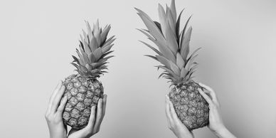 Two hands each holding a ripe pineapple against a yellow background.