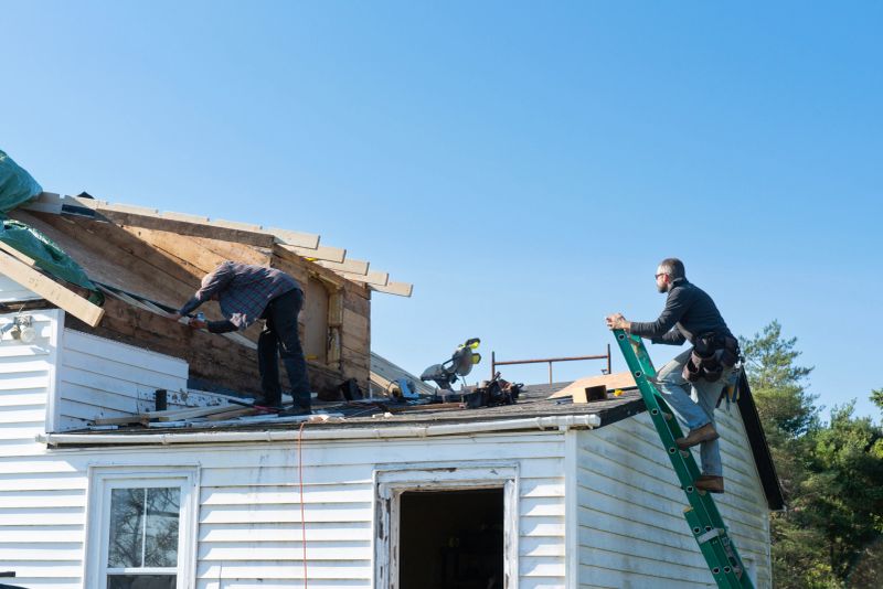 An exterior photograph of an older home undergoing a renovation. Men are working on the roof.
