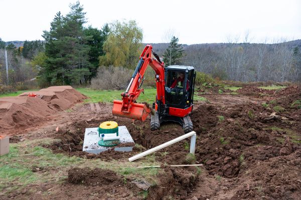 A man operates a red excavator installing a septic tank in a rural area.