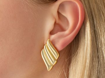 Close-up of a gold and cream-colored elegant earring on a woman's ear.
