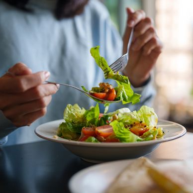 Person eating fresh salad with fork and spoon.