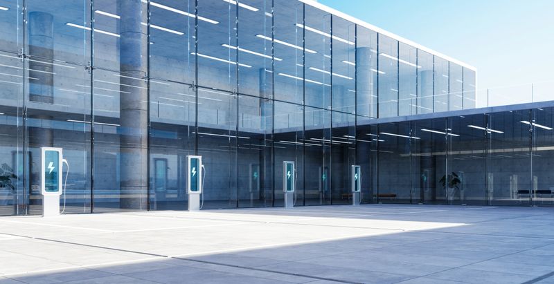 Ev charging stations stand ready outside a modern glass office building, symbolizing green energy and eco-conscious commuting. 3D rendering