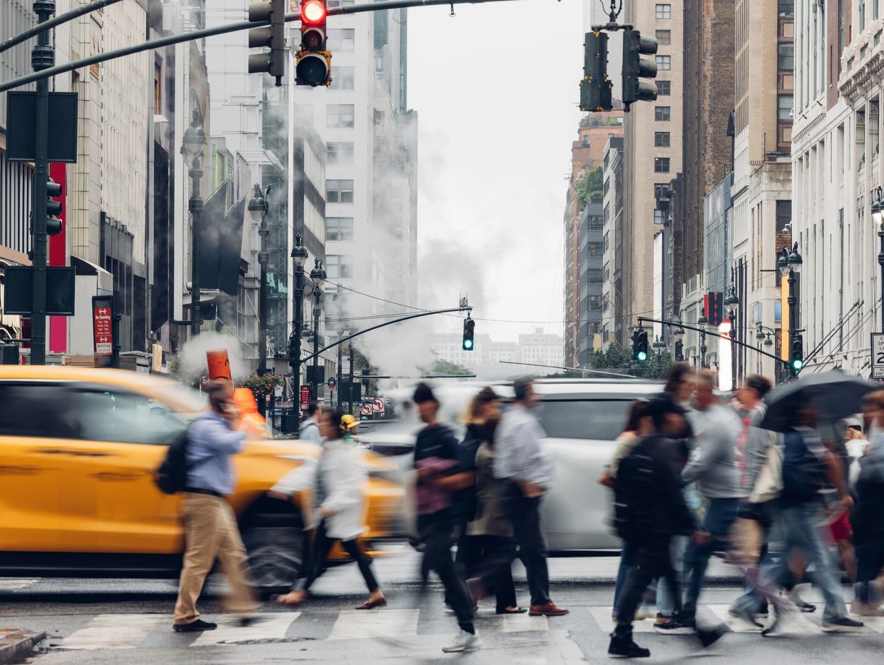 Blurred pedestrians crossing a busy urban street with yellow taxi and traffic signals.