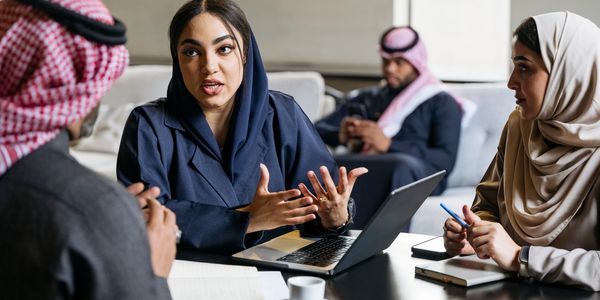 A group of Middle Eastern professionals engaged in a discussion around a table with a laptop.