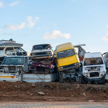 Stacked wrecked cars in a junkyard under a clear sky.