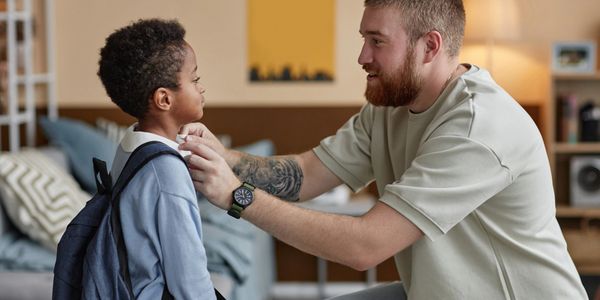 Man helping child with backpack and collar at home.