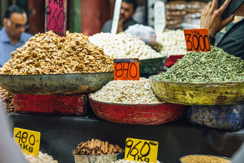 A vibrant display of spices and dry fruits in colorful containers with visible price signs at the bustling Chandni Chowk market, a hub for culinary and cultural diversity in Old Delhi, India.