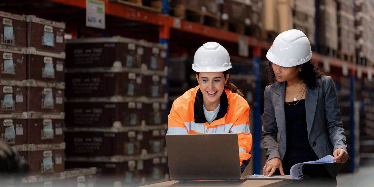 Dos mujeres con casco trabajando en un almacén.