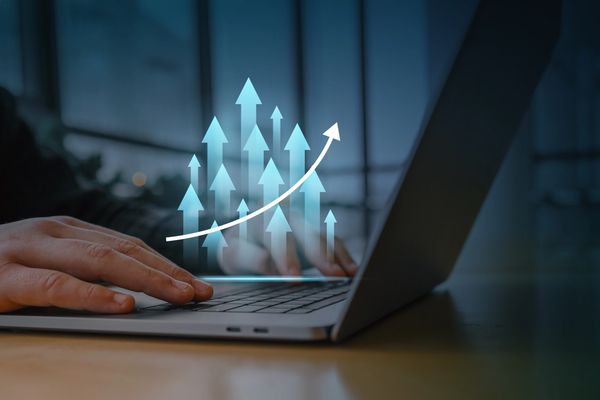 Person typing on laptop with rising arrow graphics symbolizing growth.