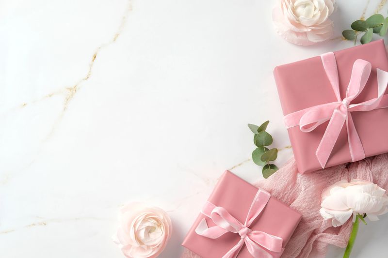 Pink gift boxes with ribbons, white flower, and green eucalyptus leaves on a marble background. Happy Mothers Day greeting card template.