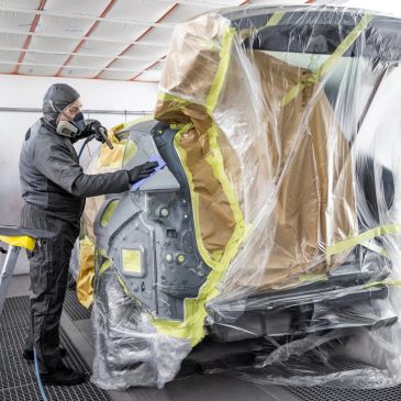 Worker applying paint protection on car part.