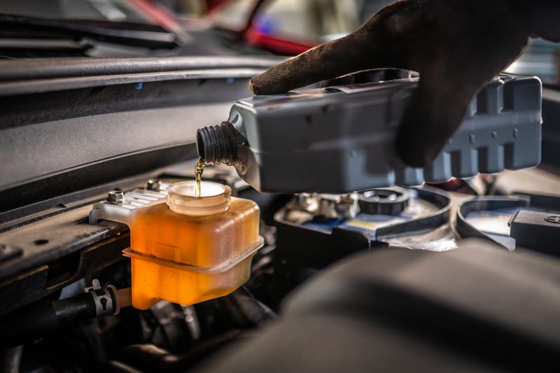A mid adult Caucasian male mechanic is seen diligently changing oil in an auto workshop. The scene highlights attentive care, technical skill, and the professional environment of vehicle maintenance. The mechanic's hands show skill and precision.