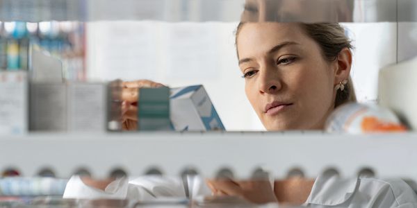 Pharmacist examining medication boxes on a shelf in a pharmacy.