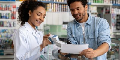 A pharmacist helps a customer review medication information at a pharmacy counter.