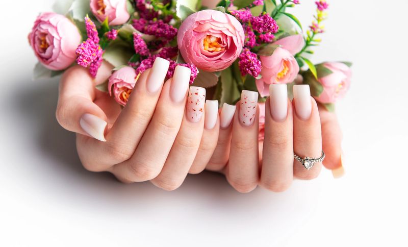 Woman showcasing her modern pink manicure while holding a bouquet of pink flowers