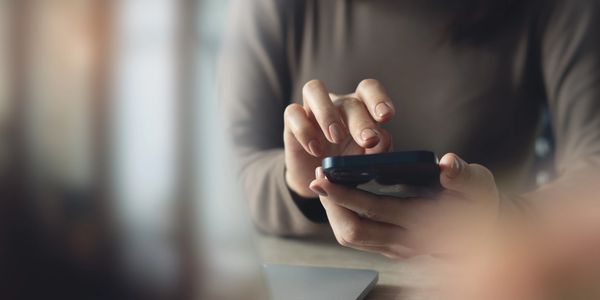 A person using a smartphone with a laptop nearby.