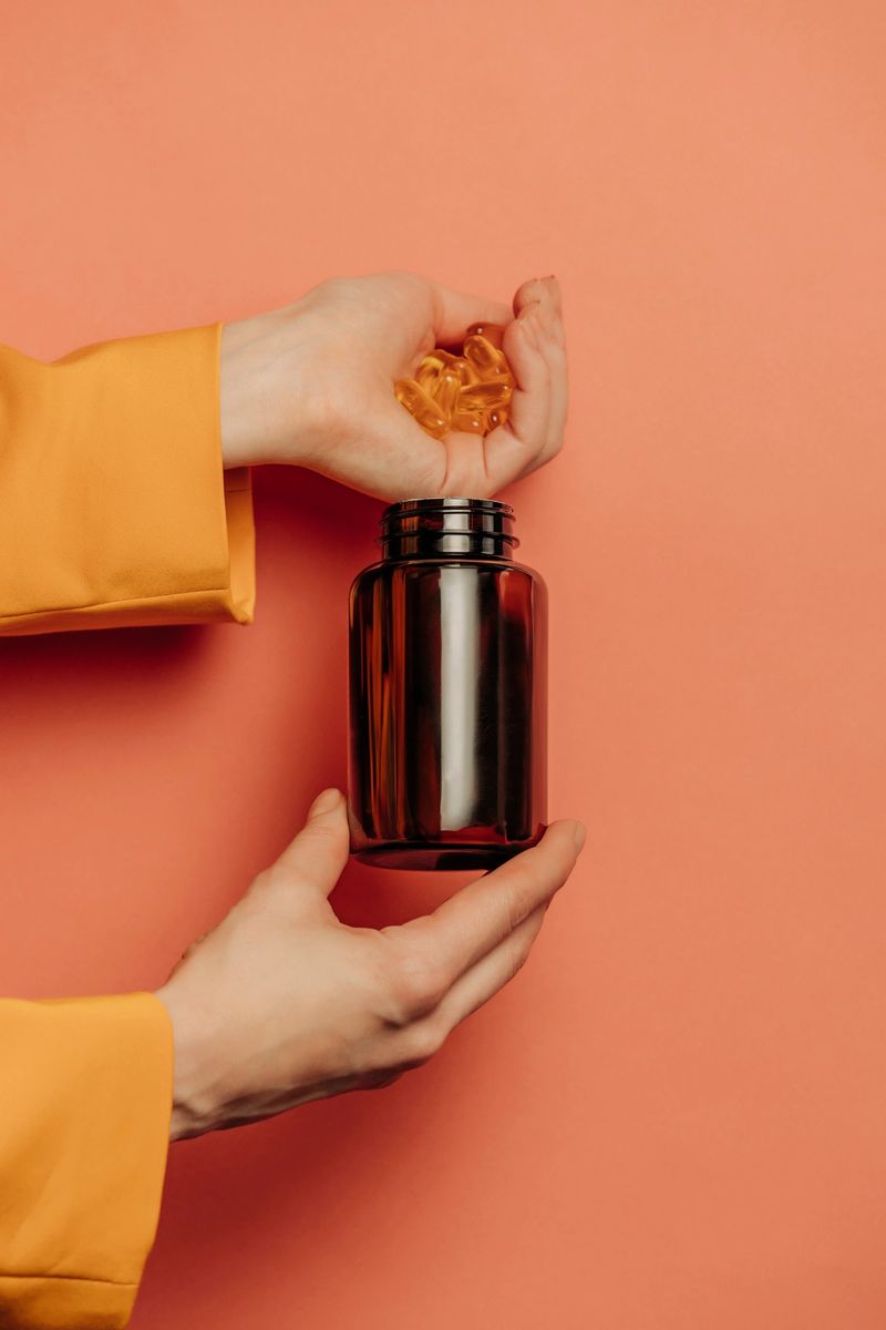 woman's hand in a yellow blazer holds vitamin capsules with fish oil against a pink background