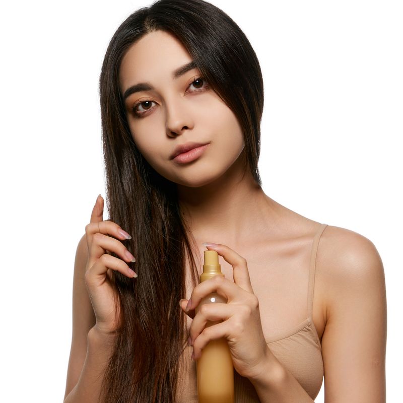 Beautiful young Korean girl taking care after hair, applying spray for hair treatment, adding shine and strength. Heat protection. Concept of natural beauty, skincare, cosmetics and cosmetology