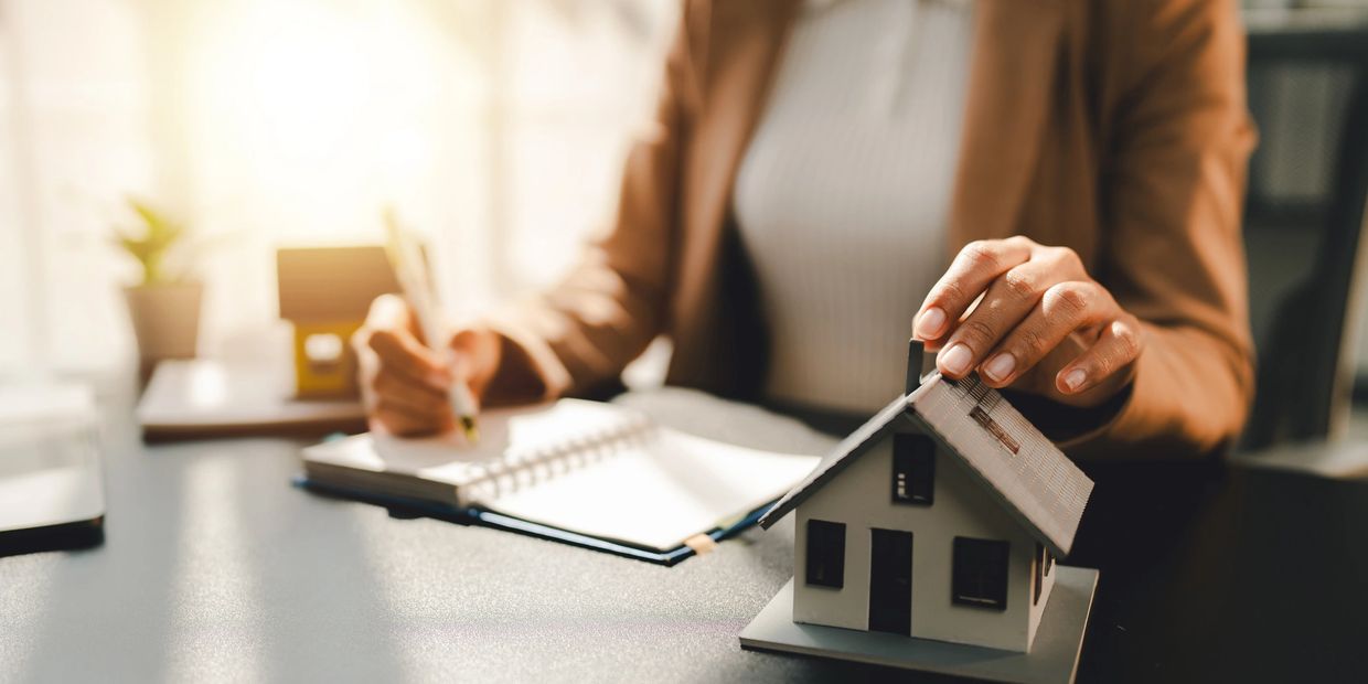 Person holding a small house model while writing in a notebook.