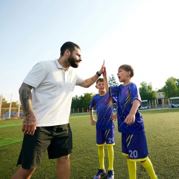 Coach high-fiving a young soccer player on the field.