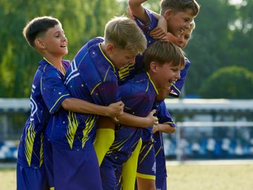 Young boys in blue sports uniforms playing and laughing together outdoors.