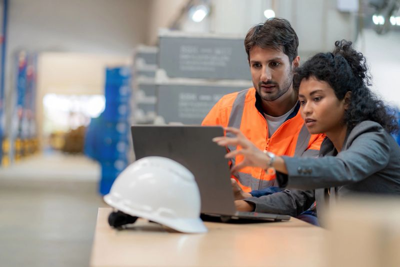 Warehouse manager and inventory controller analyzing stock data using a computer. Business strategy, supply chain efficiency, and warehouse management optimization. Logistics, teamwork, freight transportation, and digital transformation in a distribution warehouse.