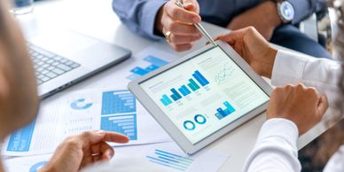 Two professionals discuss financial charts on a tablet and printed reports.