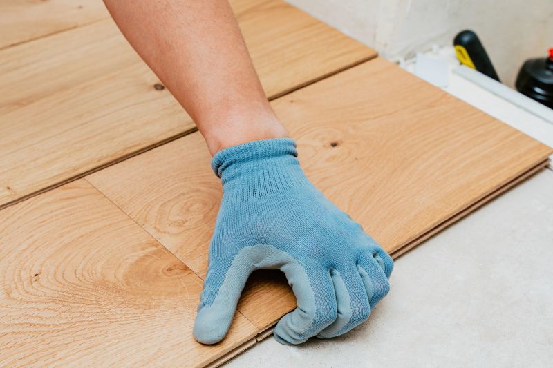 Worker installer wearing blue gloves carefully aligns wooden floor planks, ensuring smooth and accurate installation